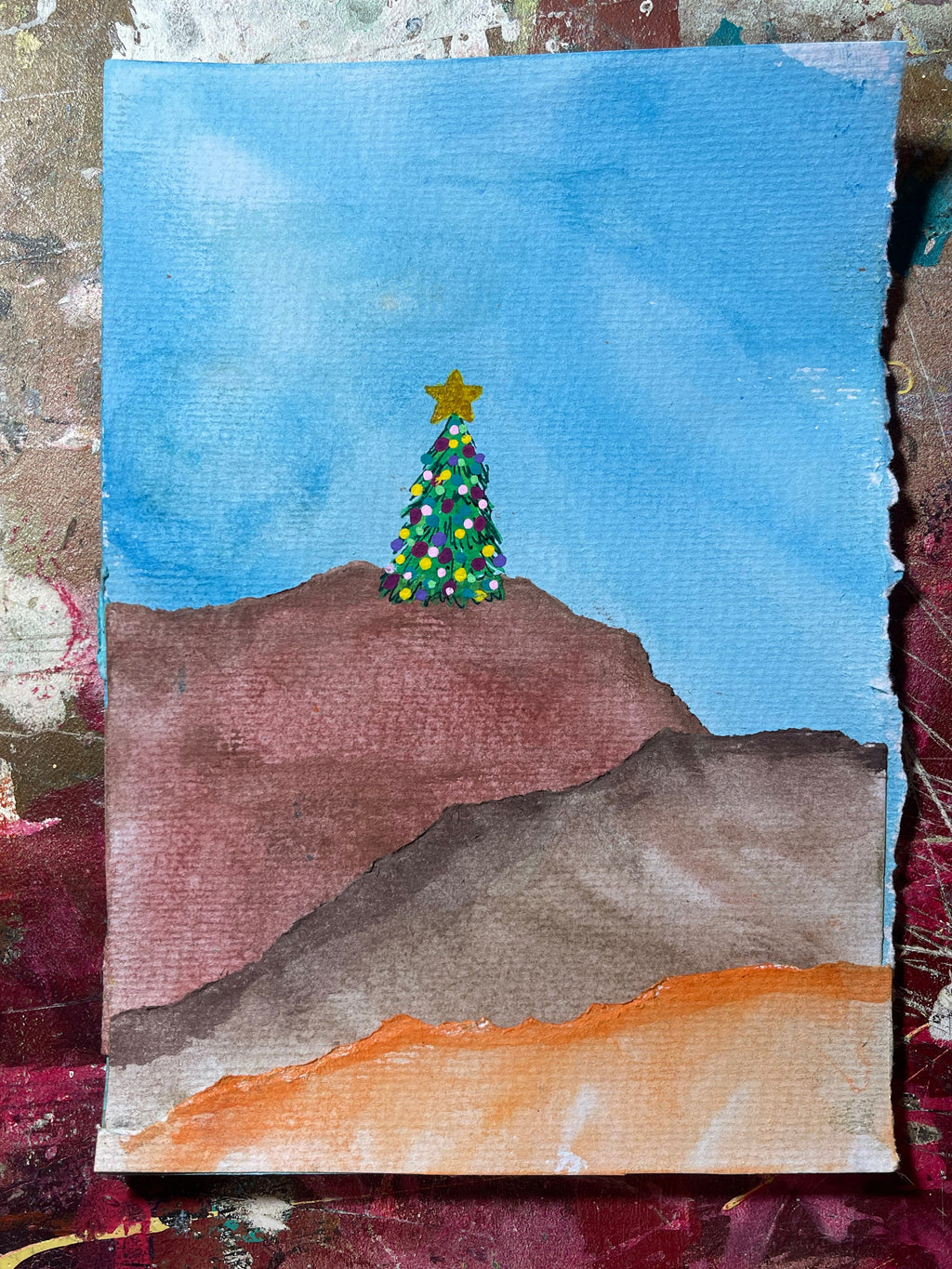 Children's drawing of a Christmas tree with a star on a blue sky background, surrounded by textured paper.