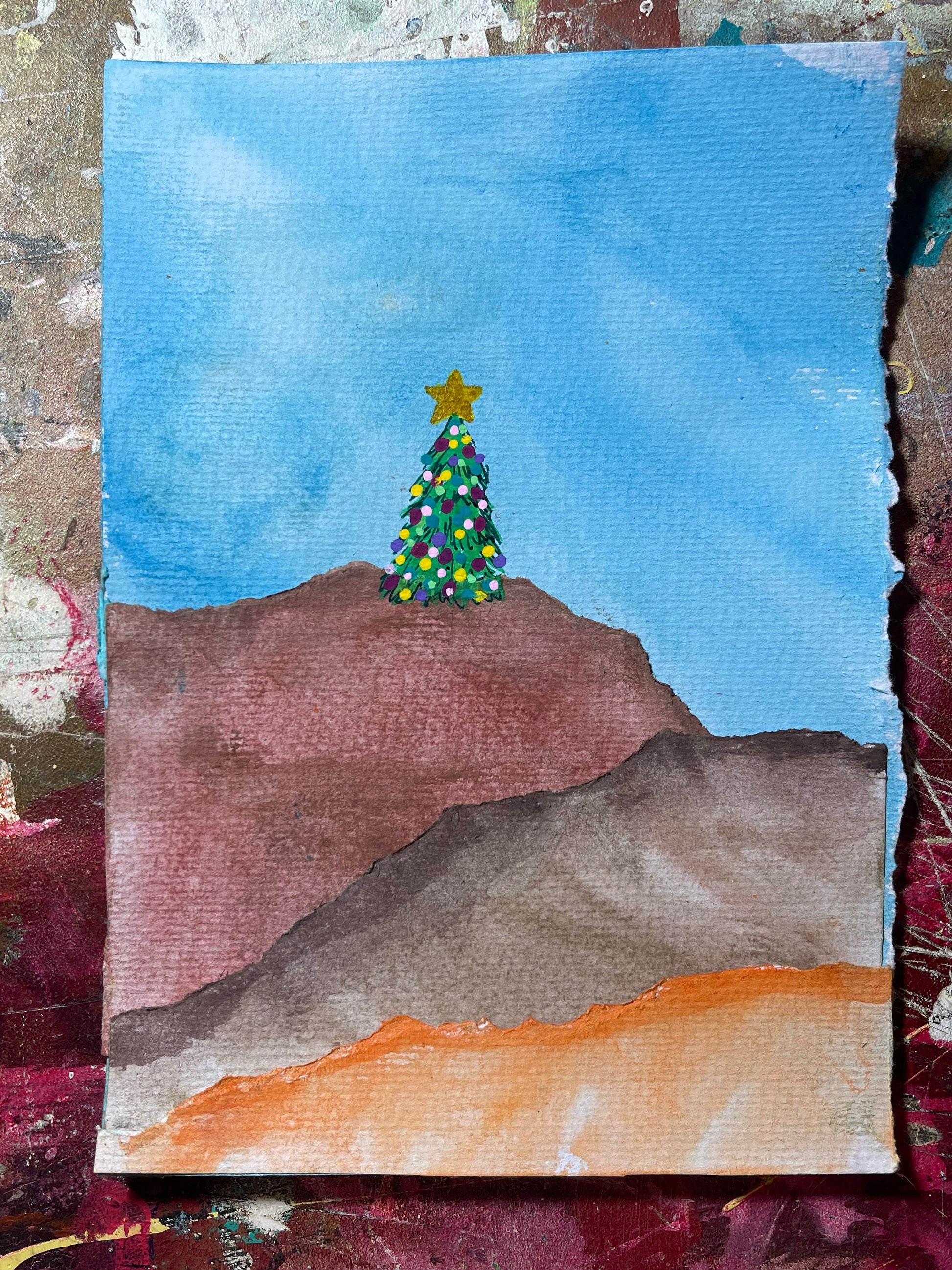 Children's drawing of a Christmas tree with a star on a blue sky background, surrounded by textured paper.