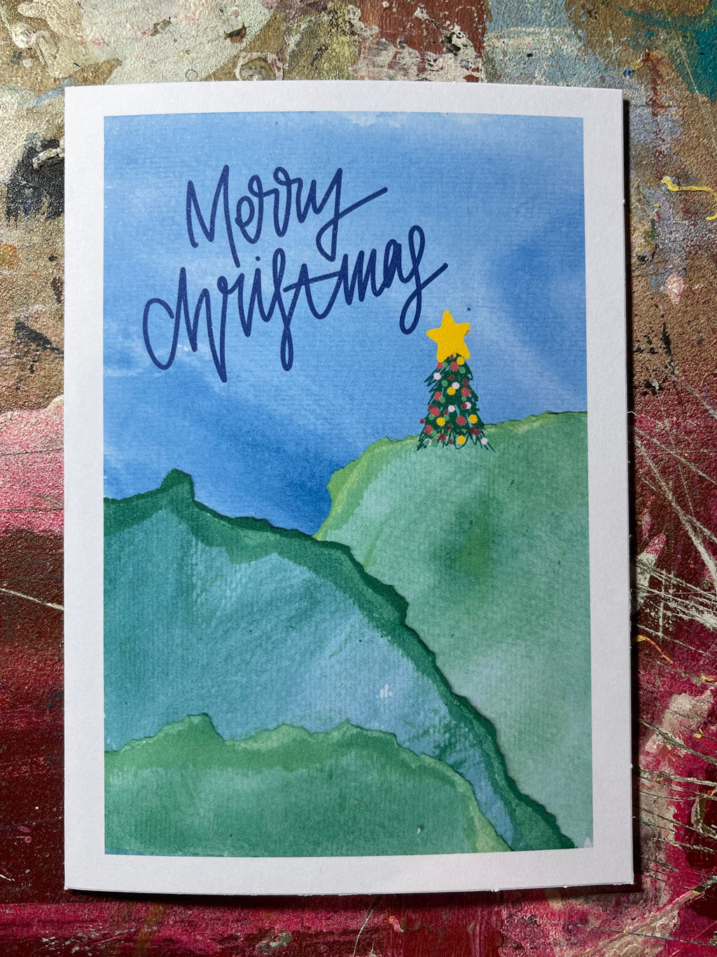 Hand-drawn Christmas card with a star and tree on a blue sky background, featuring the text 'Merry Christmas'.